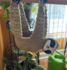 a crocheted slotty hanging upside down on a wooden rail next to a potted plant