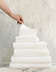 a stack of white towels being folded on top of each other in front of a marble wall