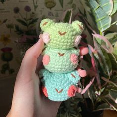 a hand holding two small crocheted teddy bears in front of a potted plant