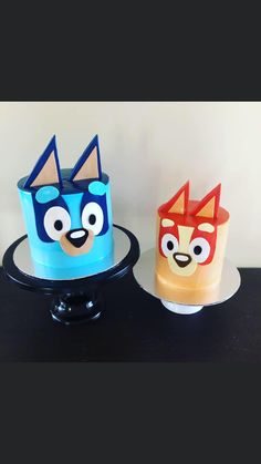 two cakes decorated to look like cartoon characters are sitting on a black table with white wall in the background