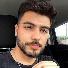 a young man with a beard is sitting in the back seat of a car and looking at the camera