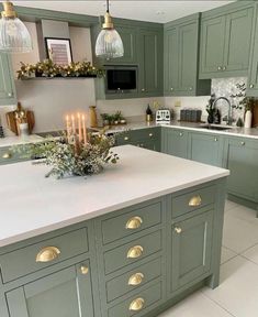 a kitchen filled with lots of green cabinets and white counter tops covered in gold pulls