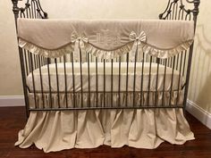 a baby crib with white sheets and ruffles on the bottom, next to a hardwood floor