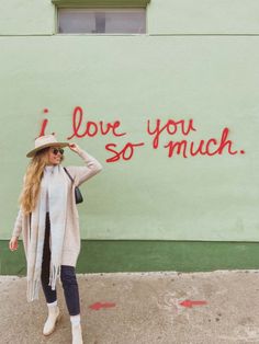 a woman standing in front of a wall that has graffiti on it and says i love you so much