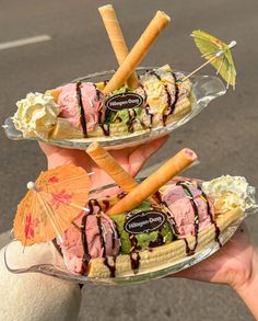 two ice cream sundaes with carrot sticks and an umbrella on the top are being held by someone's hand