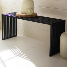 a white vase sitting on top of a wooden table next to a black metal bench