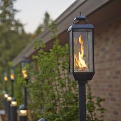 a lamp post with fire burning in it next to a brick building and shrubbery