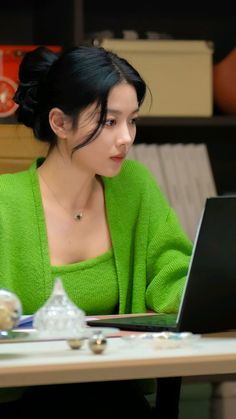 a woman sitting at a table with a laptop computer in front of her and looking at the screen