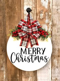 a merry christmas sign hanging on the side of a wooden fence with holly and red berries