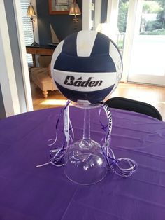 a volleyball is sitting on top of a wine glass that sits on a purple table cloth