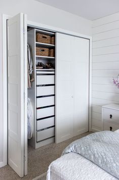 an open closet with drawers and baskets on the bottom shelf next to a white bed