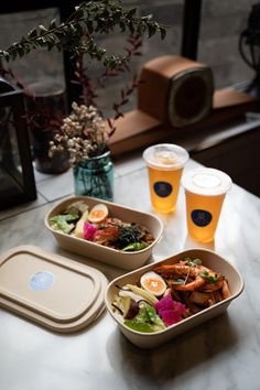 three plastic containers filled with food sitting on top of a table next to two cups