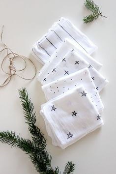 four white napkins with black crosses on them next to evergreen branches and twine