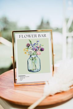 a flower bar sign sitting on top of a wooden table next to a white feather