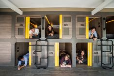 four people are sitting in bunk beds with yellow doors and numbers on the wall above them