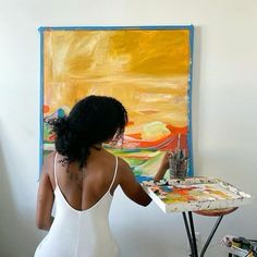 a woman in white dress painting on easel