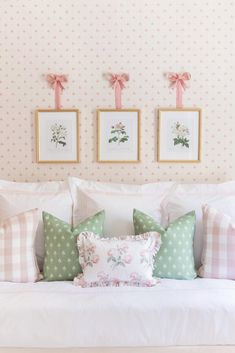 a white bed topped with lots of pillows next to two framed pictures on the wall