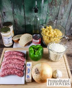 the ingredients to make this sausage and pasta dish are displayed on a cutting board, along with bread, onions, peppers, garlic, cheese, and meat