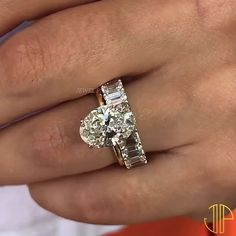 a close up of a person's hand holding an engagement ring with two stones