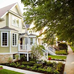 a house with white trim on the front and side of it, surrounded by greenery