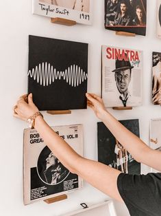 a woman standing in front of a wall covered with various records and magazine covers on it