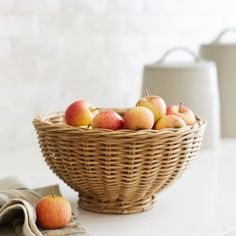 a wicker basket filled with apples on top of a white counter next to a tea towel