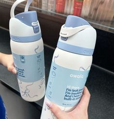 two water bottles are being held up by someone's hand in front of them