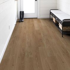 a wooden floor in front of a white door with a bench on the other side