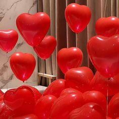 many red heart shaped balloons are floating in the air near a marble wall and drapes