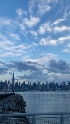 the city skyline is seen from across the water with clouds in the sky above it