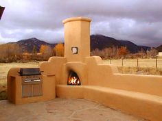 an outdoor kitchen with a fire in the middle and mountains in the background, on a cloudy day