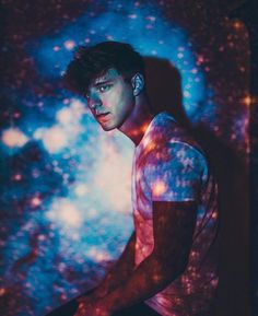 a young man is standing in front of a colorful background with stars and lights on it