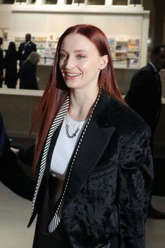 a woman with red hair is smiling at the camera while wearing a black jacket and white shirt