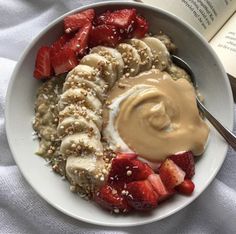 a white bowl filled with fruit and oatmeal next to an open book