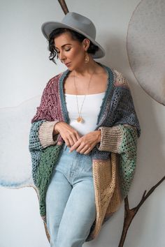 a woman in jeans and a hat leaning against a wall