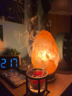 a candle is lit next to a rock on a table with a clock and alarm