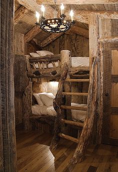 a rustic cabin with bunk beds and wooden stairs leading to the loft bed area that has a chandelier hanging from the ceiling