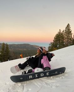 two people sitting in the snow on top of a mountain with their skis resting