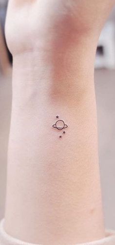 a small saturn tattoo on the back of a woman's left arm and wrist