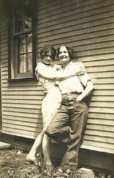 an old black and white photo of two people hugging each other in front of a house