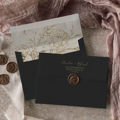 two black envelopes with gold foil stamping on them and one has a wax seal