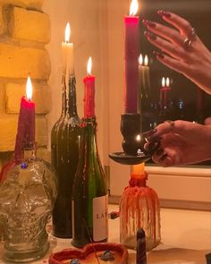 two people are lighting candles in front of bottles and glassware on a counter top