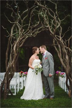 a bride and groom kissing in front of an arch made of branches at their wedding