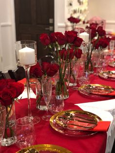 the table is set with red roses and gold place settings for two people to sit at