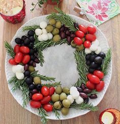 a white plate topped with olives, tomatoes and pine needles on top of a wooden table