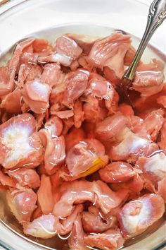 a glass bowl filled with meat sitting on top of a table next to a spoon