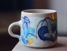 a coffee cup that has been painted with blue and yellow designs on it, sitting on a table