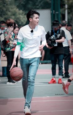 a young man holding a basketball while walking on a court with other people behind him