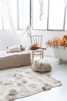 a white room with a chair, rug and flower pot on the floor in front of a window