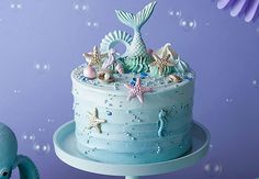 there is a blue cake with stars and mermaid decorations on it, next to an octopus figurine